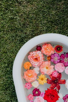 浴缸中漂浮着五颜六色的花朵，置于户外草地上，营造出宁静而艺术的场景
