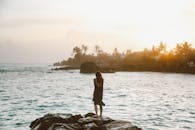 Woman in Black Tank Top and Black Pants Standing on Rock Near Body of Water during