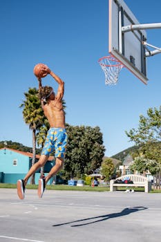Shirtless man executes a dunk on a sunny Avila Beach outdoor court.