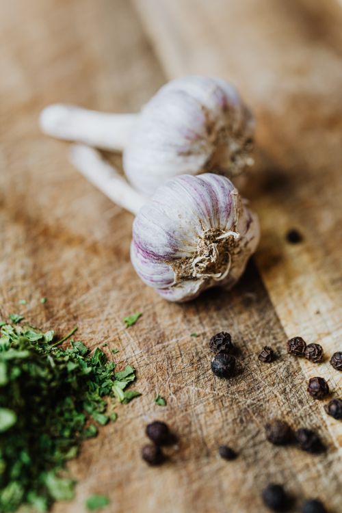 Free Close-up of fresh garlic bulbs, chopped herbs, and peppercorns on a wooden board. Stock Photo