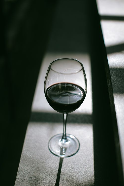 Free A glass of red wine casting intriguing shadows on a textured surface. Stock Photo