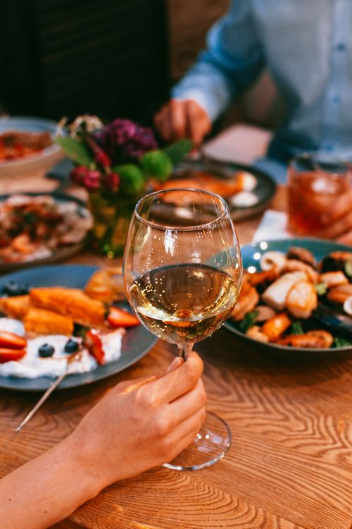Free Close-up of a wineglass in a sophisticated dining setting with diverse dishes on a wooden table. Stock Photo