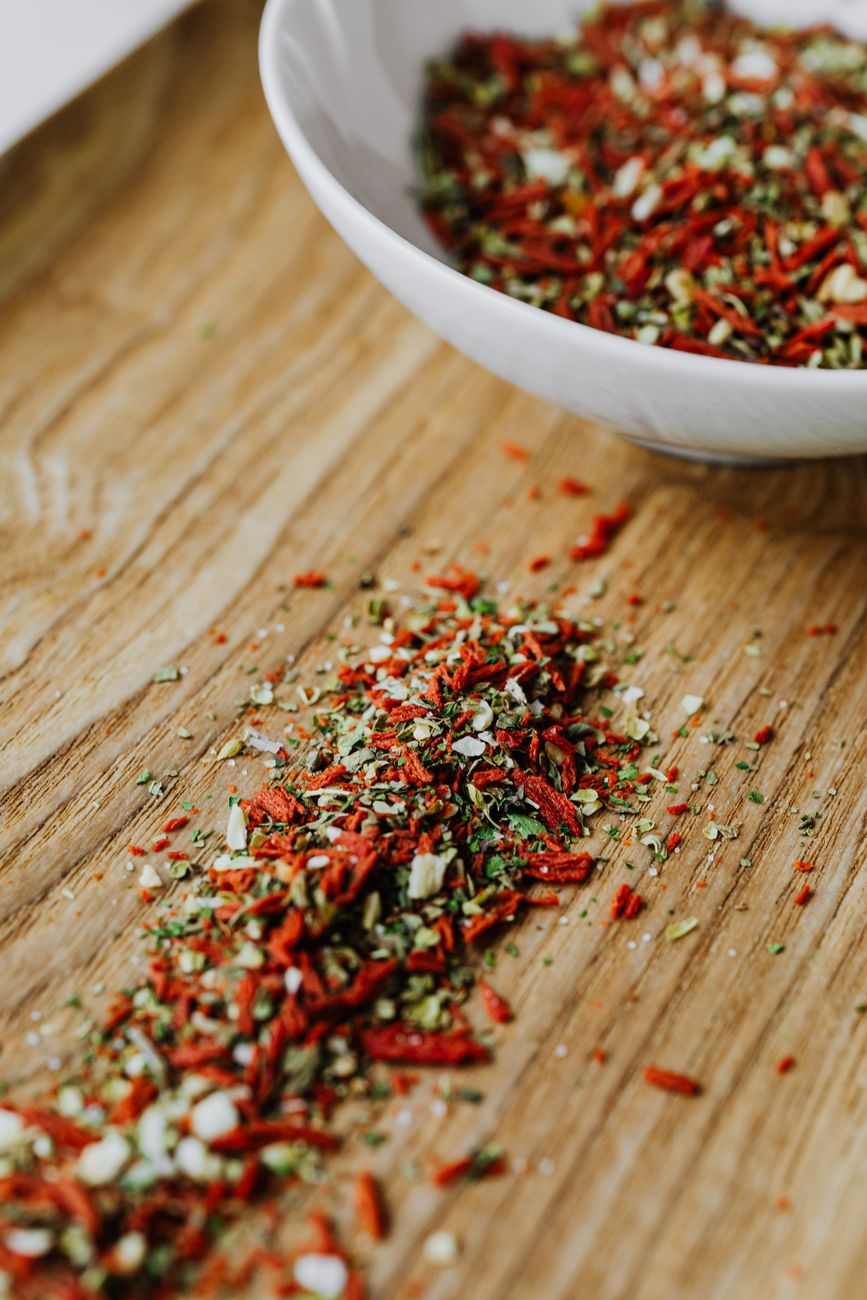 Small bowls of red harissa paste and green za'atar spice blend with berbere spices scattered on a wooden cutting board