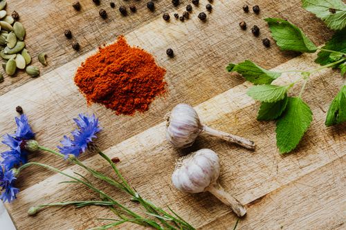 Free Fresh garlic, paprika, lemon balm, and cornflowers arranged with peppercorns on a rustic wooden board. Stock Photo
