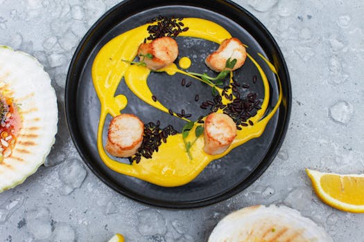 A beautifully plated gourmet scallop dish with vibrant yellow sauce and garnishes.