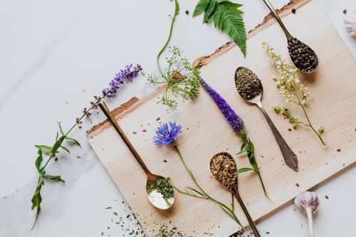 Free An artistic flat lay of herbs and flowers with teaspoons on a wooden board, perfect for culinary and health themes. Stock Photo