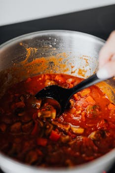 Close-up of a homemade vegetable tomato sauce being stirred in a pot with a spoon.