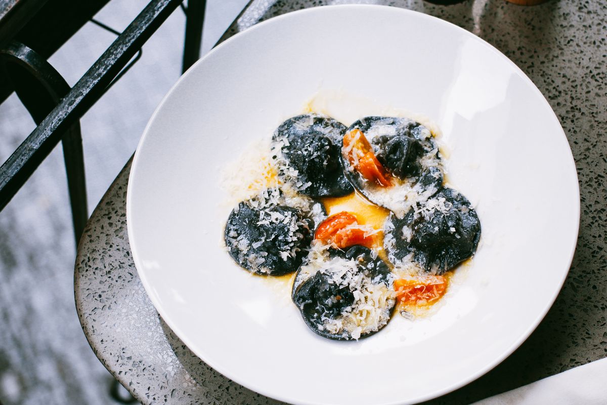 Black squid ink ravioli dusted with grated parmesan and roasted tomato pieces in a white bowl