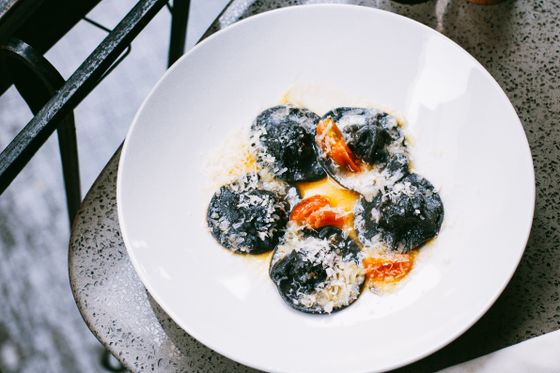 Black squid ink ravioli dusted with grated parmesan and roasted tomato pieces in a white bowl