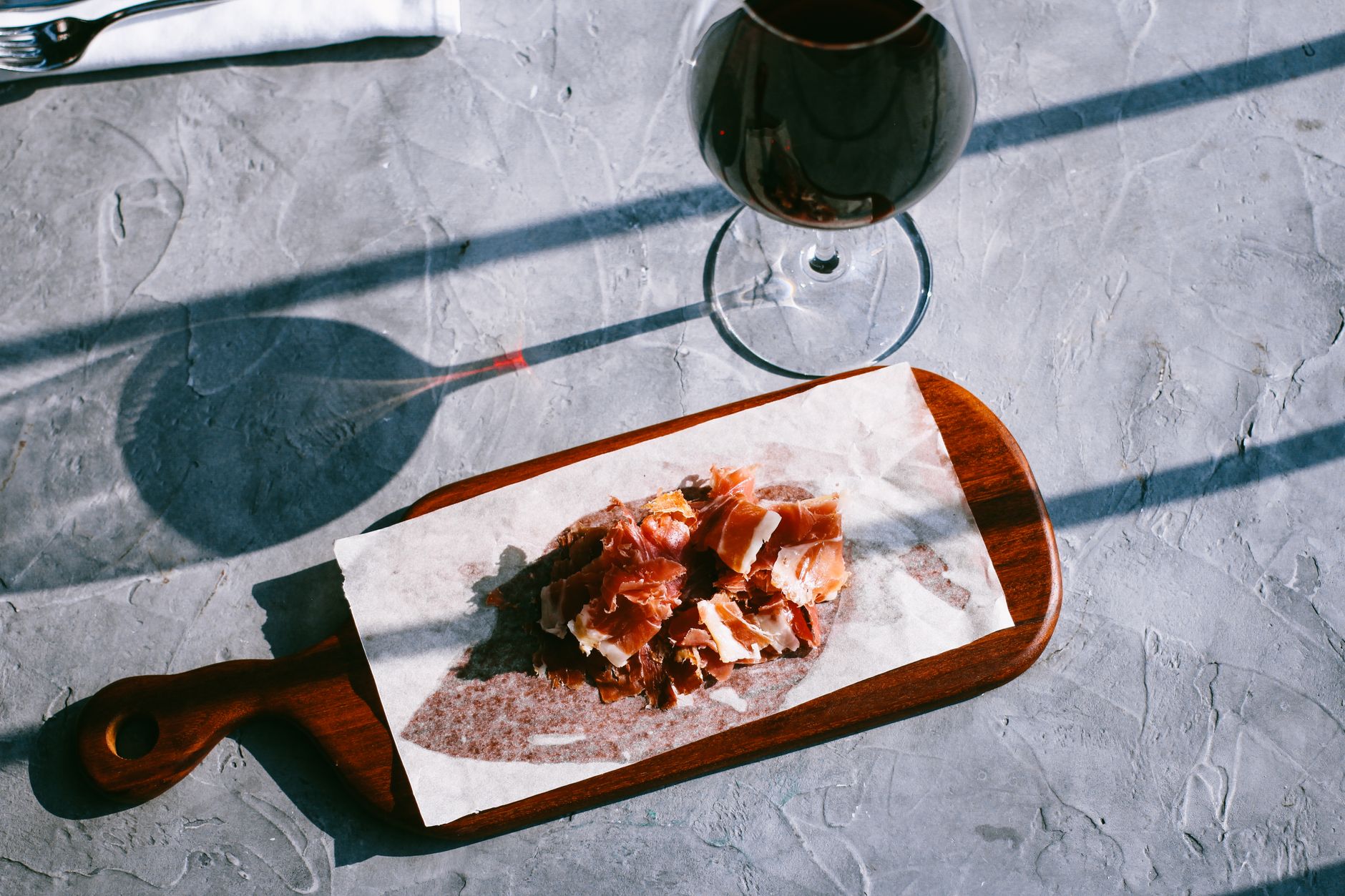 Sliced ham on a wooden cutting board paired with red wine, portrayed in warm, natural lighting.