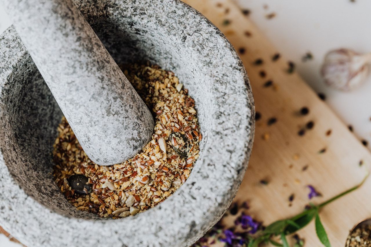close up of ground spices in a stone mortar and pestle on a wooden boa