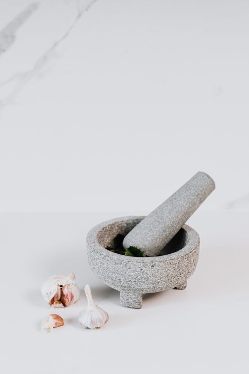 Free Close-up image of a stone mortar and pestle with garlic cloves on a marble surface. Stock Photo