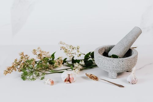 Free A minimalist setup featuring a stone mortar and pestle with garlic and herbs on a neutral background. Stock Photo