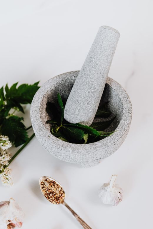 Grey granite mortar and pestle with fresh herbs, garlic and spoon