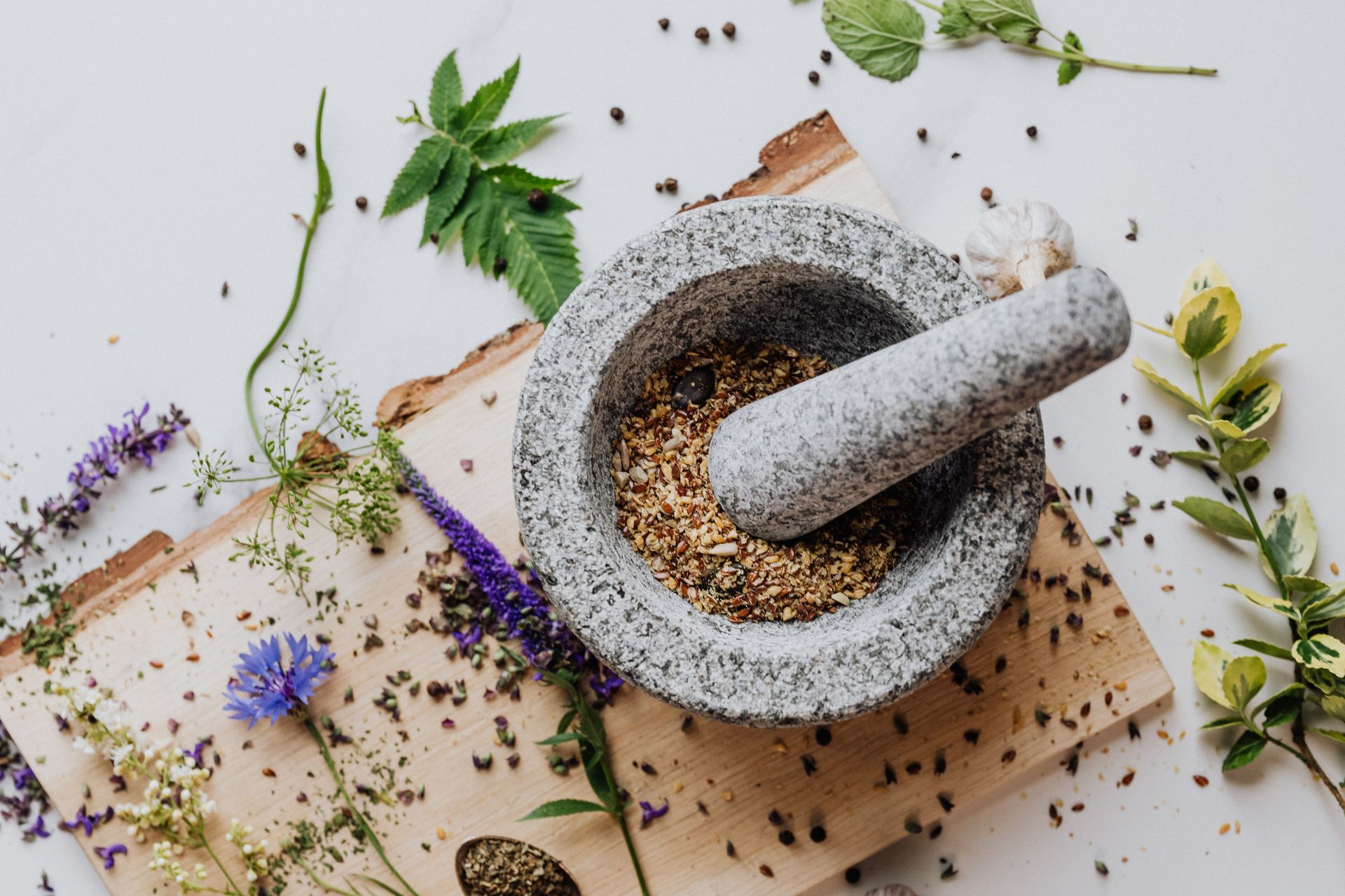 A stone mortar and pestle with herbs and leaves scattered on a wooden board, perfect for culinary and herbal imagery.