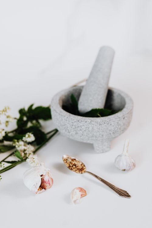 Free Stone mortar and pestle with garlic, herbs, and grains on a white background. Stock Photo
