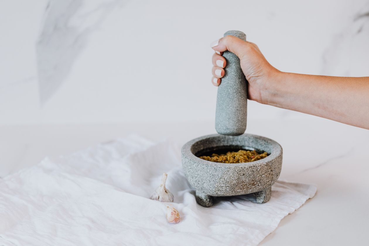 Hand using a stone mortar and pestle to grind fresh herbs and garlic into pesto