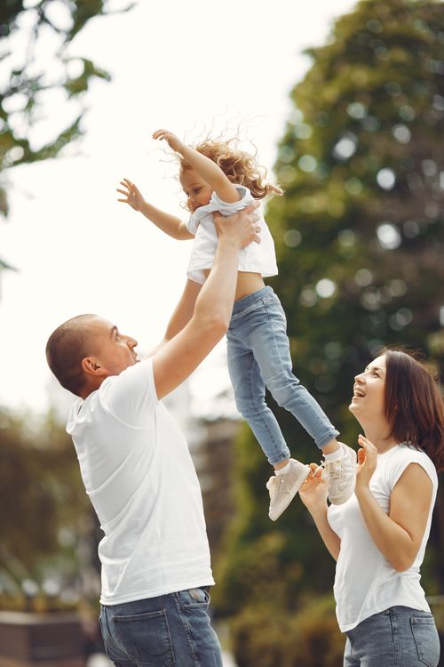 Free Joyful parents playing with their daughter in the park during a sunny day, embodying family love. Stock Photo