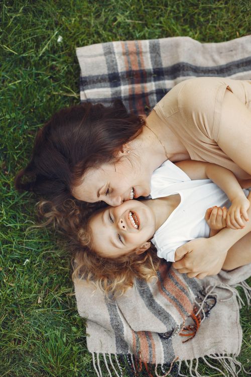 Free Mother and daughter laughing and hugging on a blanket outdoors, enjoying quality time together. Stock Photo