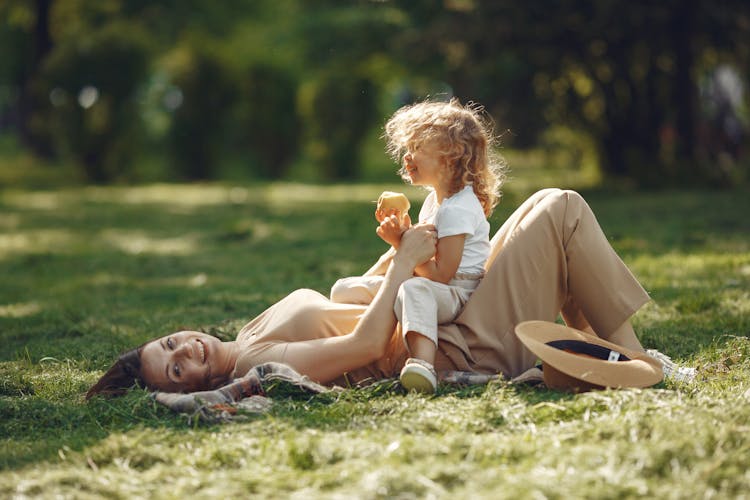 Selective Focus Photo Of A Mother Lying On The Grass While Playing With Her Child