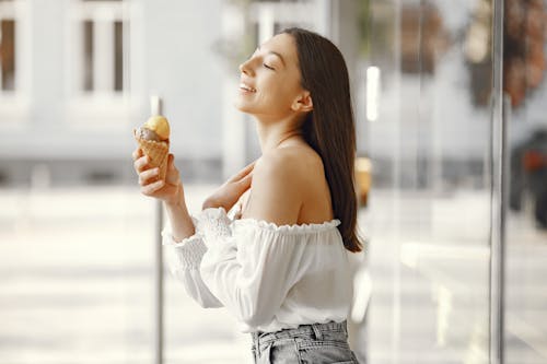 Selective Focus Photo of a Woman in a White Off Shoulder Top Holding an Ice Cream