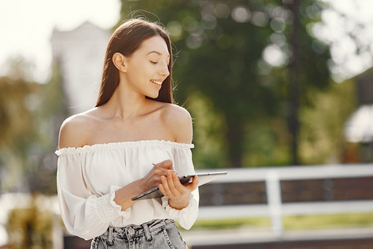 A Woman In White Off Shoulders Holding An Ipad