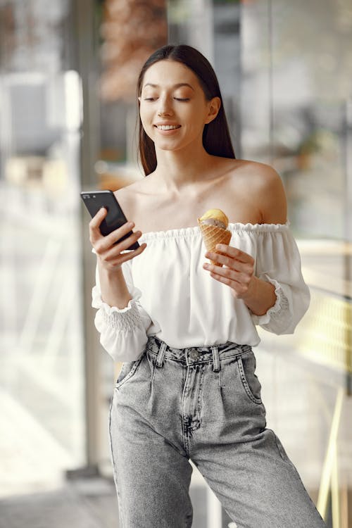 Photo of a Girl Holding an Ice Cream Cone and Her Cell Phone