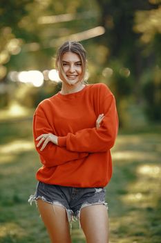 Casual portrait of a smiling woman in nature, wearing an orange sweatshirt and denim shorts