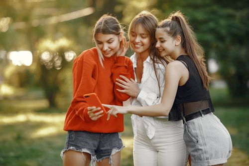 Free Three young women smiling and taking a selfie together in a sunny outdoor park setting. Stock Photo