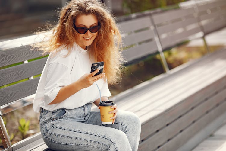 Woman Sitting On Bench With Coffee And Phone