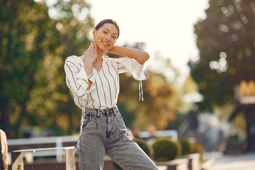 一名年轻女子穿着时尚的条纹衬衫和牛仔裤，在户外微笑着摆姿势