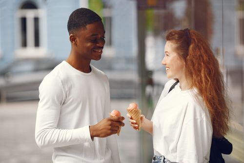Free Smiling interracial couple enjoying ice cream cones together outdoors. Stock Photo