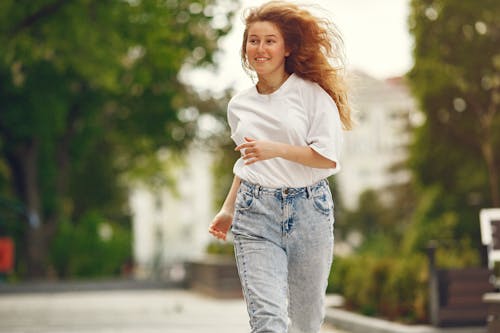 A Woman in White Crew Neck T-shirt and Blue Denim Jeans Running on the Park