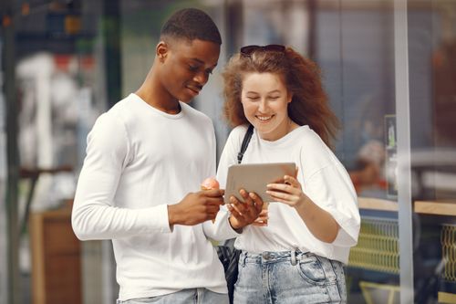 Free Happy interracial couple smiling while using a tablet and enjoying ice cream in an outdoor setting. Stock Photo