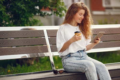 Woman In White T-shirt And Blue Denim Jeans Sitting On White Wooden Bench