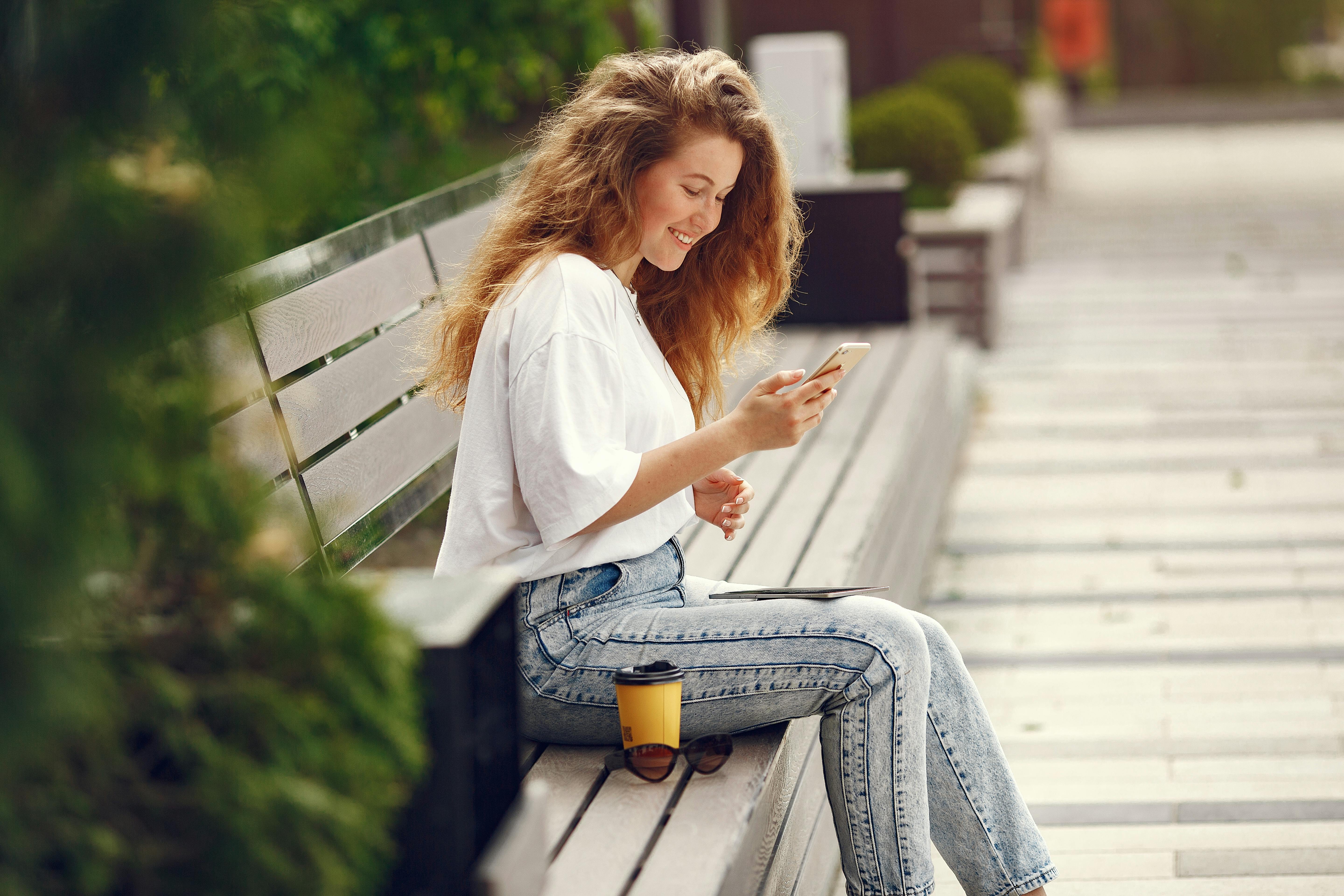 Woman in White Shirt and Blue Denim Jeans Sitting on Wooden Bench