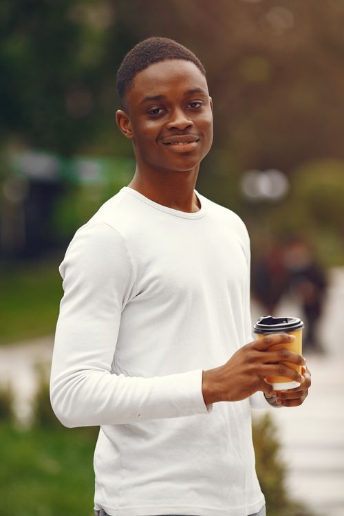 Free A young man smiling while holding a coffee cup in a park setting. Stock Photo