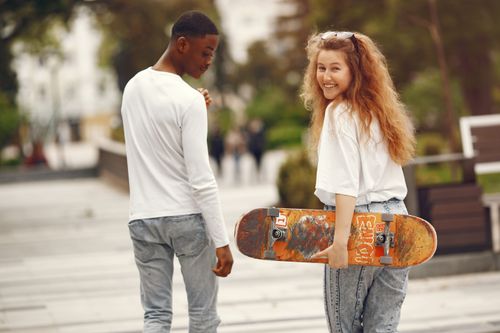 Free Happy interracial couple skateboarding in the park, enjoying a bright sunny day together. Stock Photo