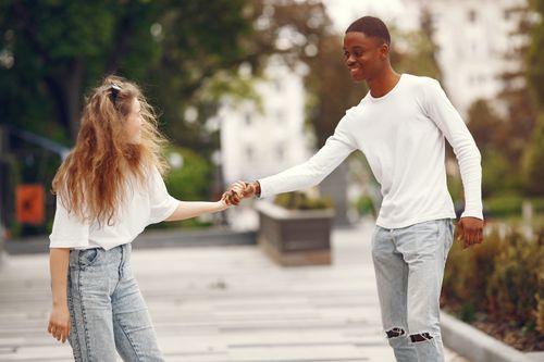 Free Smiling interracial couple enjoying a walk outdoors, holding hands and wearing casual outfits. Stock Photo