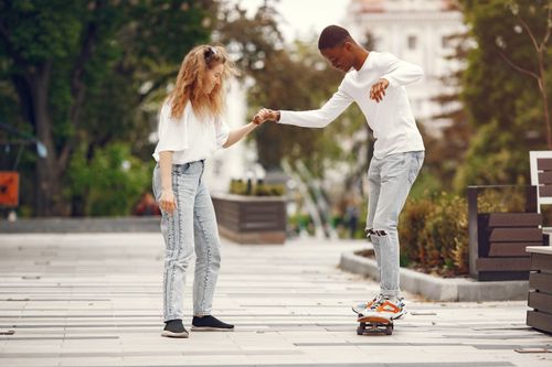 Free Happy interracial couple skateboarding together in a park on a sunny day, enjoying outdoor activities. Stock Photo