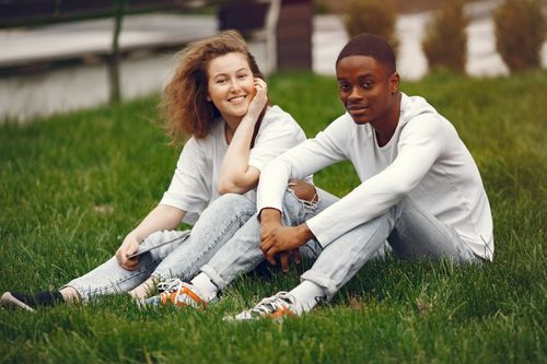 Free Happy young couple sitting together on grass and smiling outdoors. Stock Photo