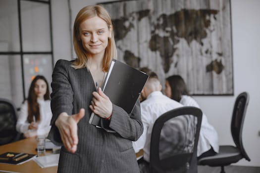 Professional woman offering a handshake in a vibrant office setting, symbolizing teamwork and collaboration.