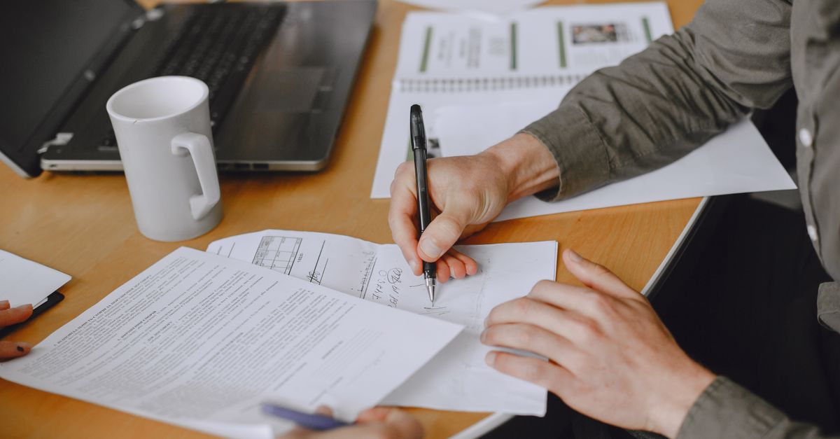 Two people signing a printed agreement at a table next to an open laptop