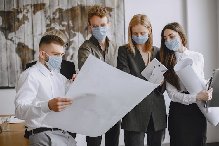 Employees In Facemasks Discussing Paper In Office