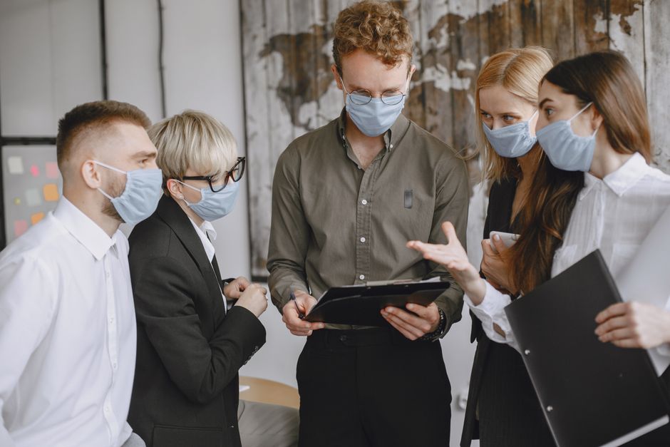 Grupo de profesionales usando mascarillas discutiendo estrategias en interiores.