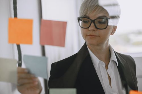 Free Woman in suit reviewing colorful sticky notes on office board, reflecting focus. Stock Photo