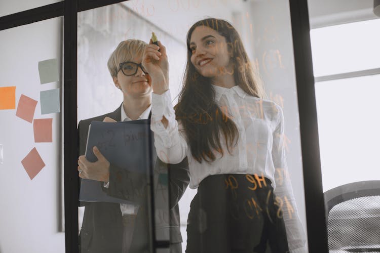 Women Writing Business Proposals With Marker On Glass