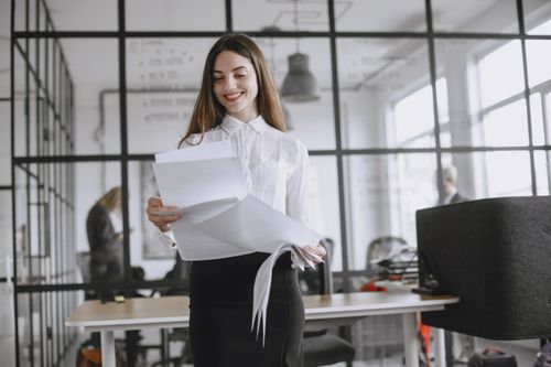 Free Confident woman with long hair reviewing documents at modern office desk. Stock Photo
