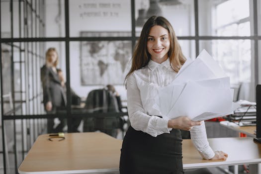 一位穿着白衬衫的自信年轻女子，在现代办公环境中拿着文件微笑