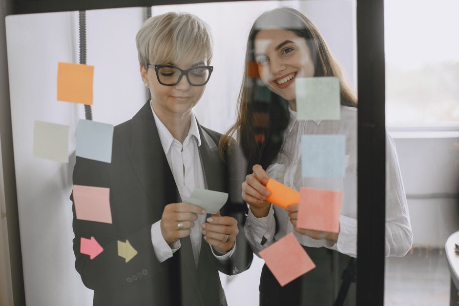 Two women collaborate in a modern office, using colorful sticky notes for brainstorming.